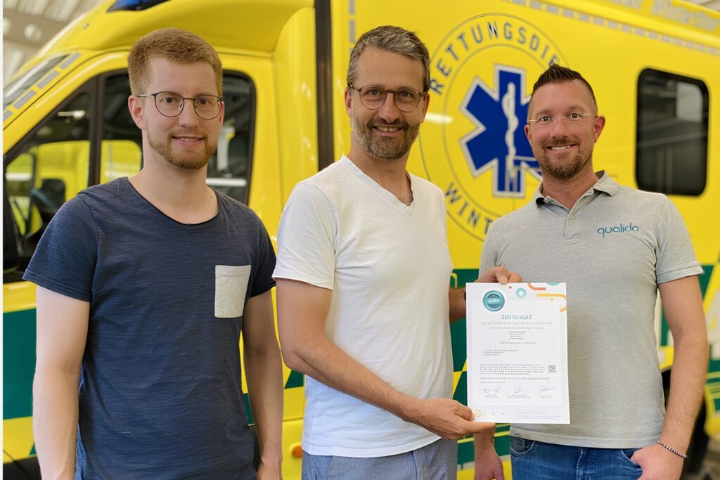 Übergabe eines Zertifikats nach einem Workshop beim Rettungsdienst Winterthur, im Hintergrund ein gelber Rettungswagen.
